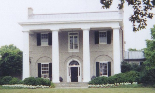 Picture of a two story Greek Revival with grey stucco and four white columns in front porch.